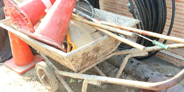 A wheelbarrow filled with construction tools and orange traffic cones.