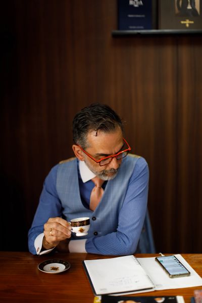 Man in glasses drinking coffee and looking at phone on desk.