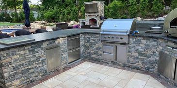 Modern outdoor kitchen with stone finish and stainless steel appliances.