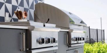 Modern outdoor kitchen with stainless steel grills and geometric tile backsplash.