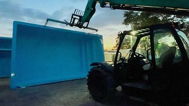 A machine lifting a large blue pool shell at dusk.