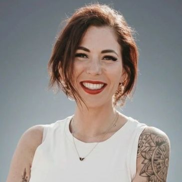 Smiling woman with tattoos and white sleeveless top.