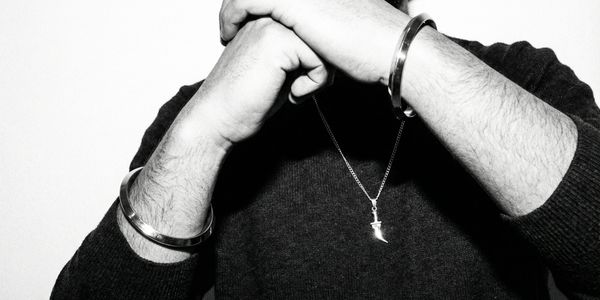 Person with hands clasped wearing a pendant and bracelets.