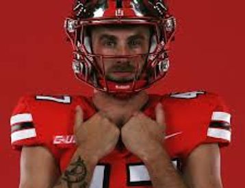 Football player in red jersey with helmet and tattoos posing.