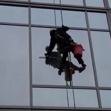 Window cleaner suspended on ropes washing glass on a tall building.
