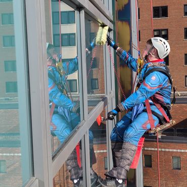 Window cleaner in superhero suit cleans building facade while suspended.