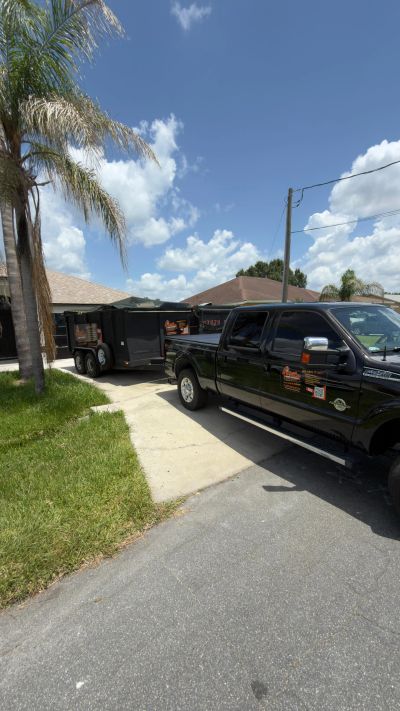 Black pickup truck towing a trailer in a driveway under a blue sky.