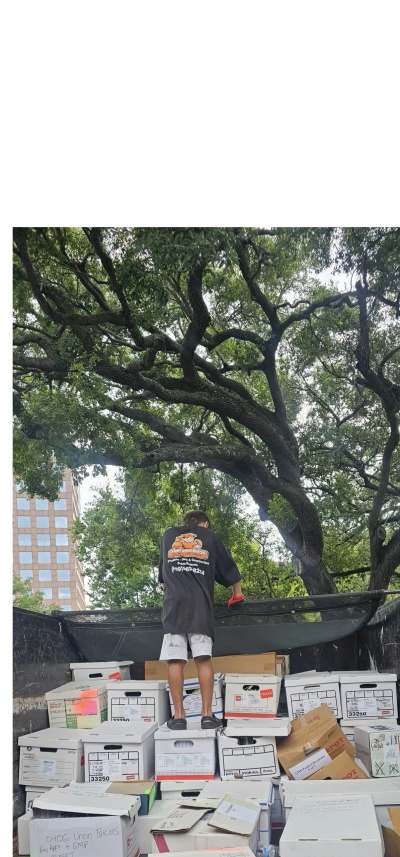 Person standing on stacked boxes outdoors under trees.