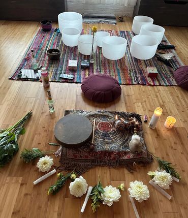 Picture of sound bowls, candles, flowers, on a rug.