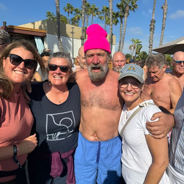 Three women standing with Wim Hof with some people in the background.