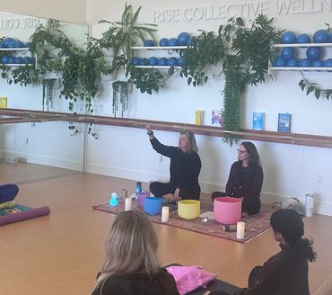 Picture of two women seated with sound bowls in front and other women seated in the foreground