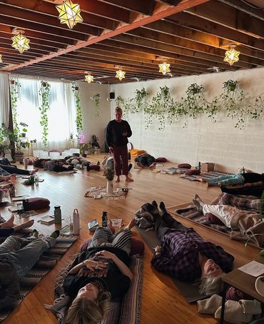 Picture of a studio with instructor standing in the middle of people laying down on yoga mats.