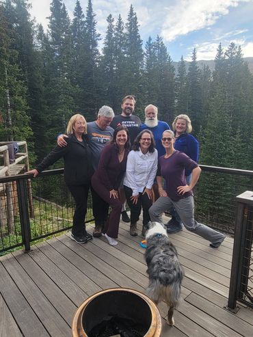Picture of 8 people and a dog standing on a porch with mountains behind