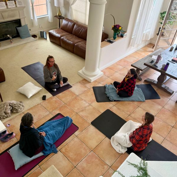 Four people sitting on mats in a living room.