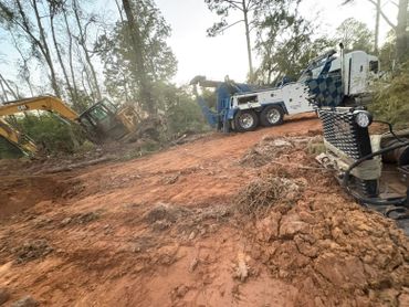 A tow truck and excavator working to pull a stuck vehicle from muddy terrain.