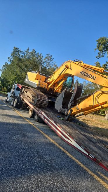 Yellow Hyundai excavator loaded on a tilted flatbed trailer attached to a semi truck.
