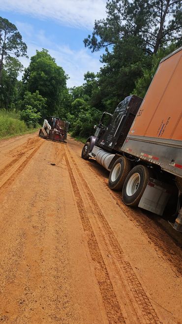 A large truck stuck on a dirt road with a skid steer loader nearby.