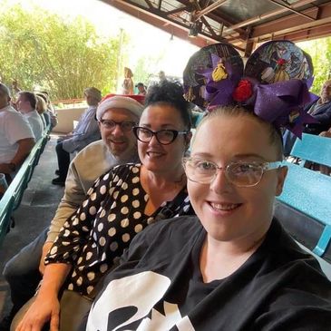 Three people smiling in a stadium with festive accessories and casual clothes.