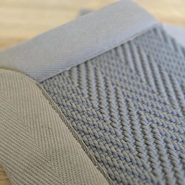 Close-up of a folded gray woven fabric with a herringbone pattern and solid borders.