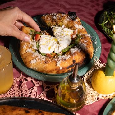 Hand picking up a slice of cheesy pizza with fresh greens on a rustic table.