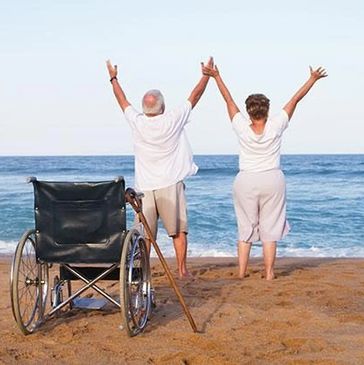 A wheelchair and cane in the foreground with a couple with their arms raised in front of the ocean