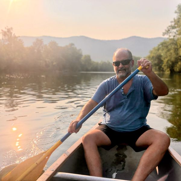 Man paddling a canoe on a calm lake at sunset.