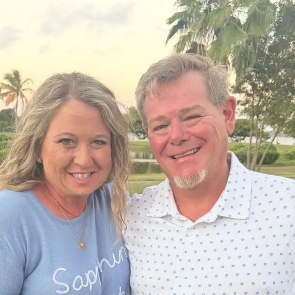 Smiling couple posing outdoors near palm trees at sunset.
