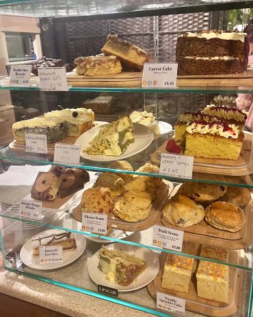 Glass display case showing various cakes, scones, and brownies with price tags.