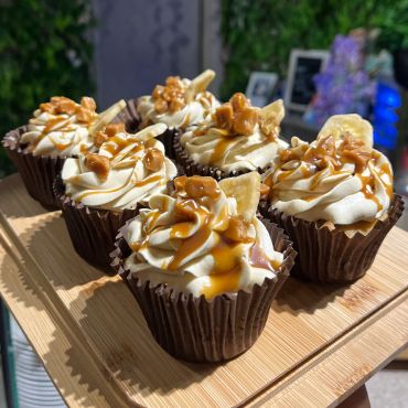 Caramel-topped cupcakes with nuts and banana chips on a wooden board.