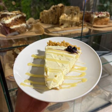 Slice of cheesecake with honey drizzle and berries on a white plate.