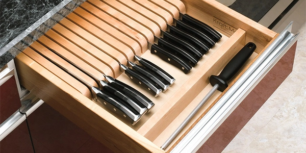 A neatly organized kitchen drawer with knives and a sharpening rod.