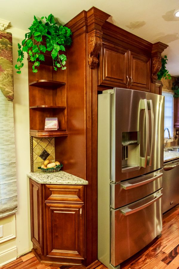 Stainless steel refrigerator with ornate wooden cabinetry and granite countertop in kitchen.