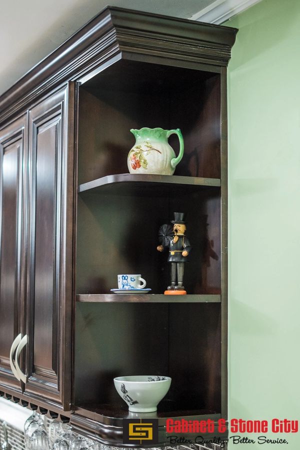 Dark wood kitchen cabinet corner shelf with decorative items and green wall.