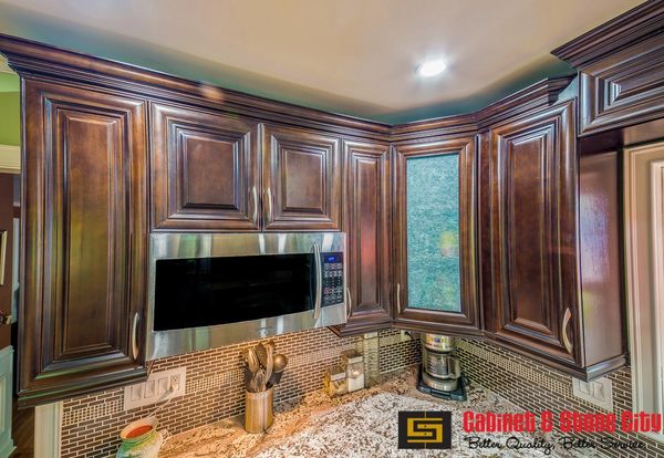 Dark wood kitchen cabinets with stainless steel microwave and granite countertop.