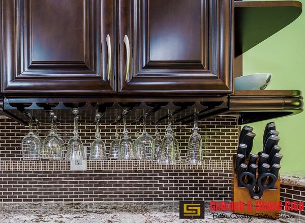 Dark wood kitchen cabinet with hanging wine glasses and a knife block.