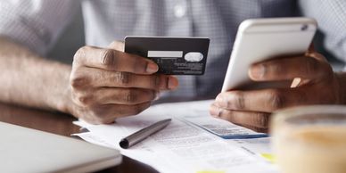 Image of a person's hands holding a cell phone and credit card over some papers on a desk