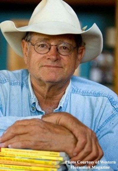 Man in a cowboy hat and glasses leaning on a stack of books.