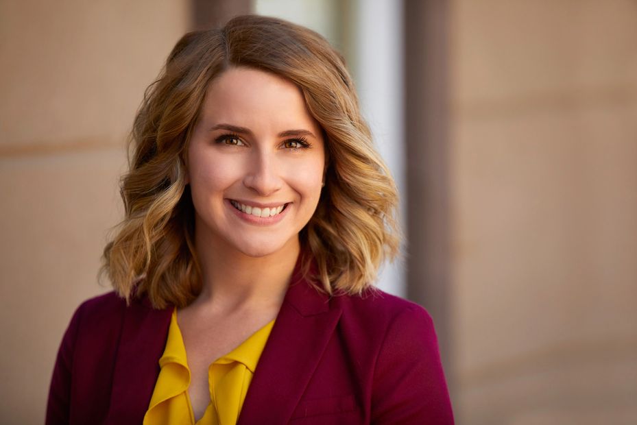 Smiling woman with blonde hair in a burgundy blazer and yellow blouse.