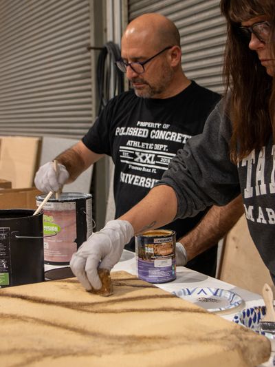 A woman and a man applying decorative stains to a concrete sample slab.