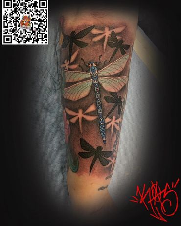Colorful dragonfly tattoo surrounded by black and white dragonfly silhouettes on a forearm.