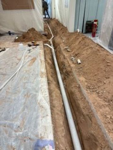 Indoor construction work with a long trench and pipe installation.