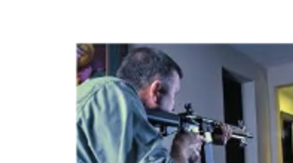 Man aiming with a rifle in an indoor setting.