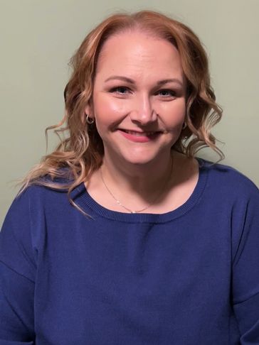 Smiling woman with curly hair in a blue sweater.