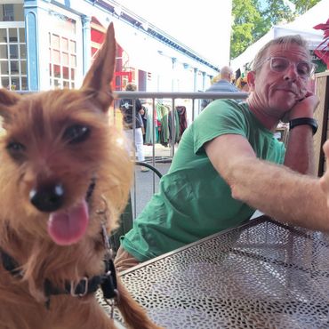 Man relaxing at outdoor cafe with dog close to camera.