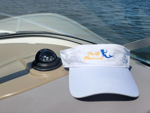 White visor cap on a boat dashboard with a compass and water in the background.