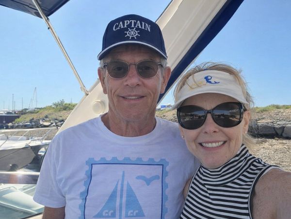 A smiling couple wearing sunglasses and hats on a boat under clear skies.