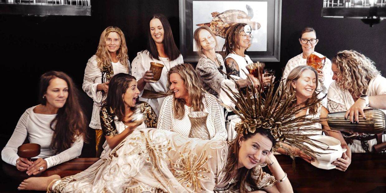 A group of women in white and gold attire holding musical instruments and smiling.