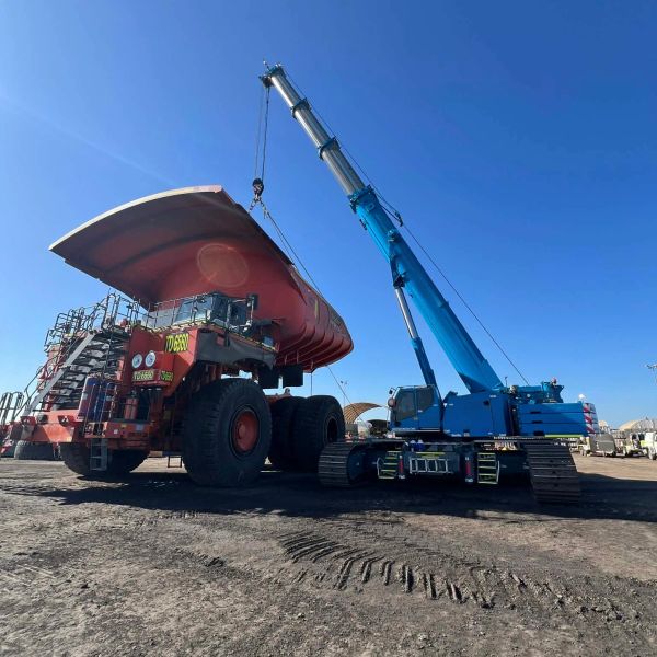 Blue crane lifting a large truck bed under a clear blue sky.