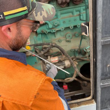 Worker in safety gear inspecting engine components closely.