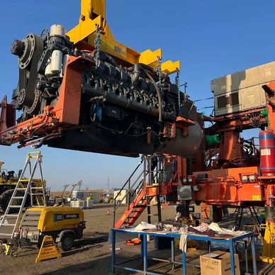 Heavy machinery engine being lifted for maintenance on a sunny day.